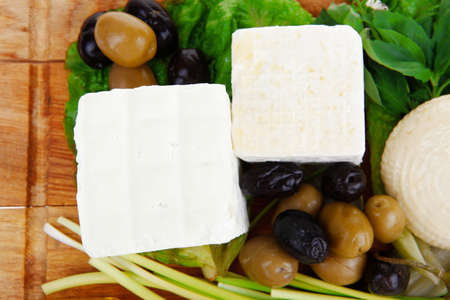 dairy food : feta white cheese cubes and round served on wooden cut plate with green leaves and olive oil isolated over white backgroundの写真素材