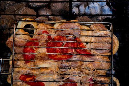 grilling spiced chicken in grid on charcoal bbq with tomatoes and vegetablesの写真素材