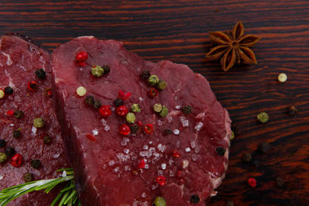fresh raw beef fillet mignon on old retro style wood as background with rosemary peppercorn and saltの写真素材