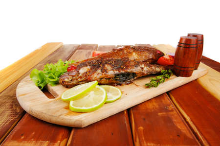 healthy food: two fried sea bass fish served with tomatoes and vegetables on big wooden board over...