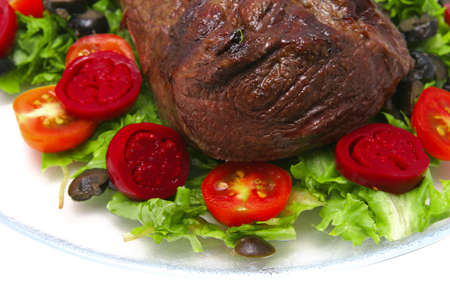 fresh ripe roasted big chunk of beef meat on green salad with tomatoes isolated on whiteの写真素材