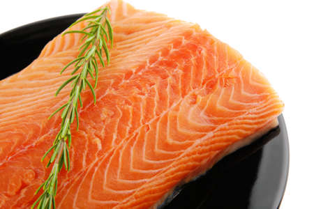 raw fresh uncooked salmon red fish fillet on black plate with rosemary twig isolated over white backgroundの写真素材