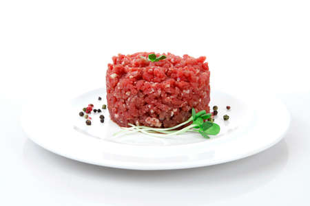 very big raw hamburger cutlet with sprouts and chilli pepper on white plate isolated over white backgroundの写真素材