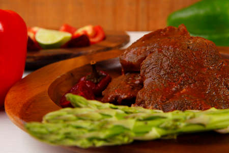 grilled roast red beef meat served on wooden dishes with peppers cutlery salad and vegetables on white wooden tableの写真素材