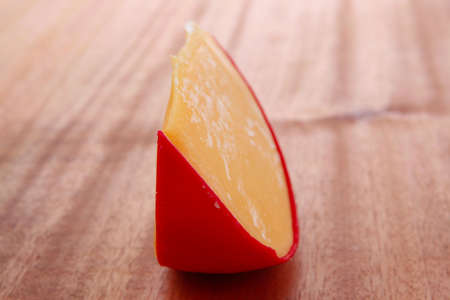 chunk of aged french cheddar cheese in hard red shell on wooden table