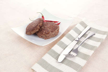 fresh juicy beef meat hamburger with dry pepper on white plate over tablecloth with cutlery