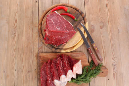 fresh raw beef meat steak and chunk with red hot pepper and dill on wooden cut plates over table