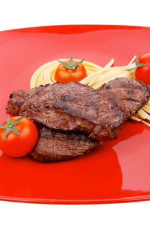 meat grilled beef steak with pasta and tomatoes on red plate isolated over white backgroundの写真素材
