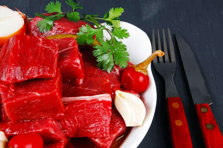 raw fresh beef meat slices in a white bowls with onion and red peppers serving on blue table with cutleryの写真素材