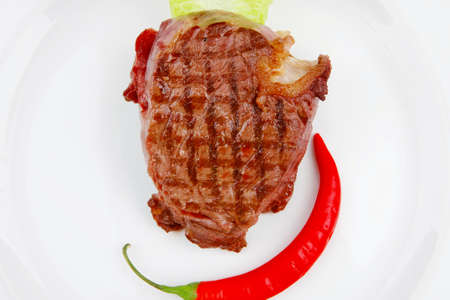 bbq : beef (pork) steak garnished with green lettuce and red chili hot pepper on white plate isolated over white backgroundの写真素材