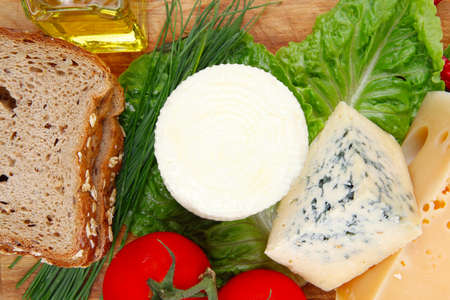 fresh aged french cheeses chops on big cutting board with tomatoes olive oil, rye breadm and green chives isolated over white backgroundの写真素材