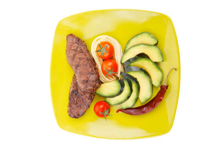 grilled meat beef steak with pasta avocado and tomatoes on green plate isolated over white...