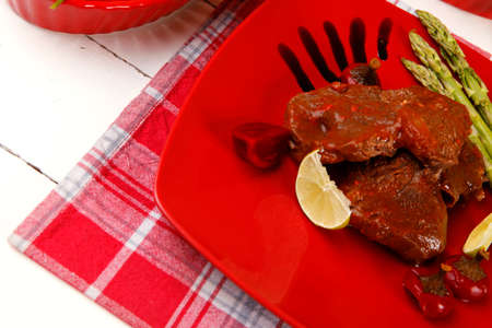 grilled beef pork meat served on red plate with asparagus hot pepper salad and bell on napkin over white wooden tableの写真素材