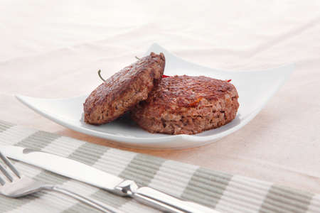 fresh juicy beef meat hamburger with dry pepper on white plate over tablecloth with cutlery