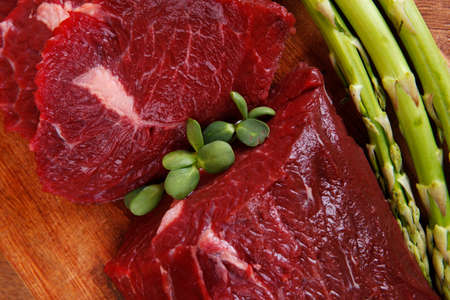 red fresh raw beef veal fillet with asparagus on cutting plate over wooden table prepared to use