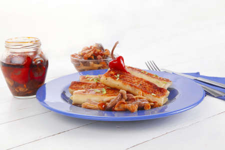 russian food - meat wrapped in a pancake with red hot pepper  and pickled mushrooms served on blue plate over wooden table in restaurantの写真素材