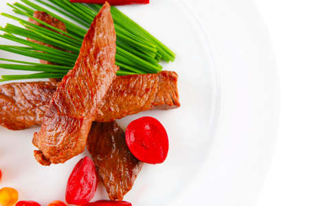 hot fresh grilled red beef meat fillet with vegetables  green chives and peppers on china plate isolated over white backgroundの写真素材