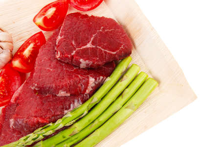 fresh raw beef meat steak fillet on wooden plate with asparagus and tomatoes ready to prepare isolated over white backgroundの写真素材