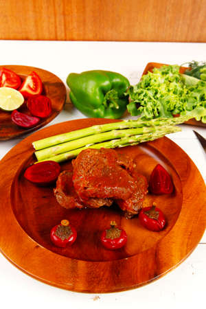 grilled roast red beef meat served on wooden dishes with peppers cutlery salad and vegetables on white wooden tableの写真素材