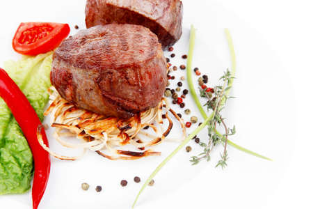 grilled beef fillet with thyme , red hot chili pepper and tomato on plate isolated over white backgroundの写真素材