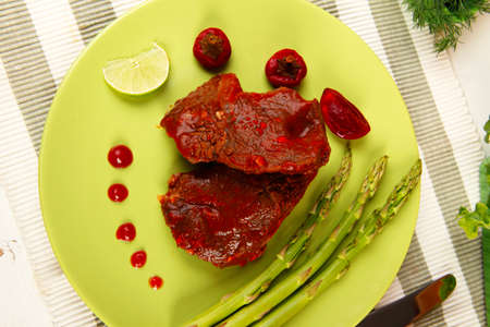 roast stew beef pork meat served with vegetables on green plate and cutlery on napkin over wooden table with red hot peppersの写真素材