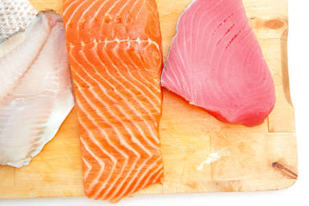 raw set of sea fish food : salmon , red tuna, and sole fish chunks served on wooden plate isolated on white backgroundの写真素材