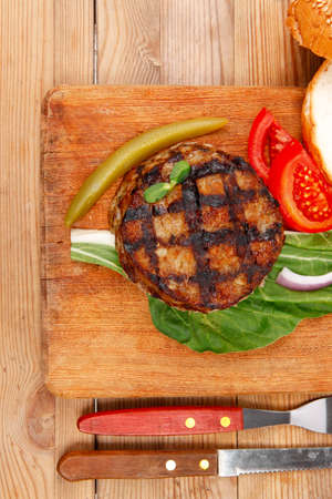 extra thick hot beef meat hamburger lunch on wooden plate with tomatoes and salad over wooden  table with cutlery and fresh sweet bunの写真素材