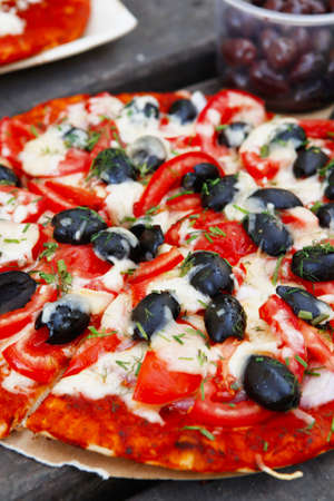 prepare hand made pizza with olives and tomatoes on wooden table on picnic with different kind of cheesesの写真素材