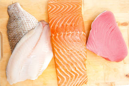 raw set of sea fish food : salmon , red tuna, and sole fish chunks served on wooden plate isolated on white backgroundの写真素材