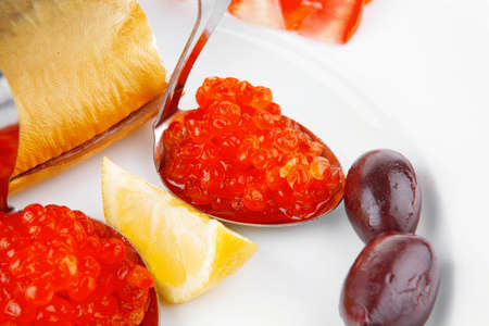 diet food - red caviar and smoked mackerel fish with lemon tomatoes and bread on white china plate isolated over white backgroundの写真素材