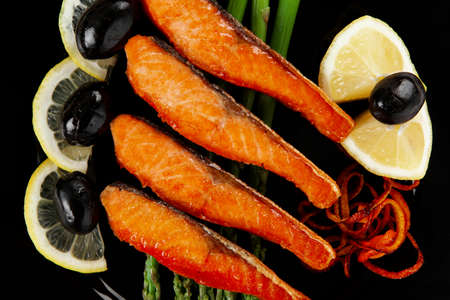 grilled salmon slices with asparagus lemon and olives on black plate isolated over white backgroundの写真素材