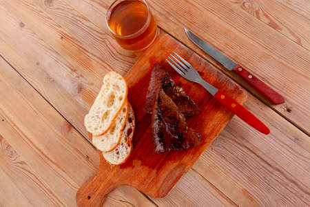 fresh beef meat steak with red hot pepper and bun slices served on plate with whiskey on wood over table with cutleryの写真素材