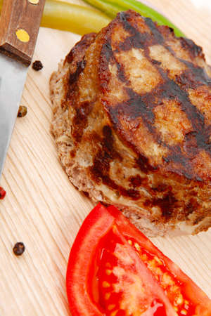 extra thick hot beef meat hamburger lunch on light wooden plate with tomatoes salad and cutlery...