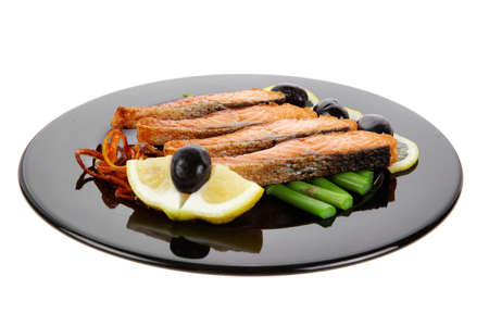 grilled salmon slices with asparagus lemon and olives on black plate isolated over white backgroundの写真素材