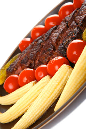 fresh red beef meat served with baby corns and cherry tomatoes on dark plate isolated on white backgroundの写真素材