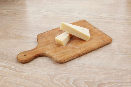 two fresh triangle french delicacy parmesan cheese pieces on wooden cut board over tableの写真素材