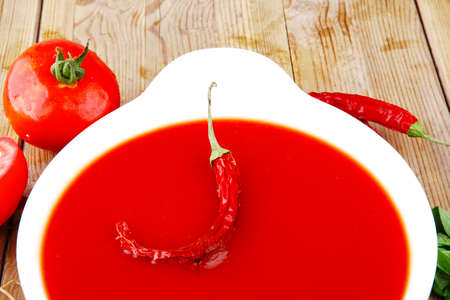 diet food : hot tomato vegetable soup with basil thyme and raw tomatoes in white round bowl over red mat on wood table ready to eatの写真素材