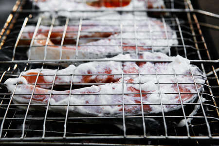 grilling salmon steak with milk cream in grid over barbecueの写真素材