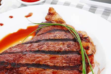 fresh rich juicy grilled beef meat steak fillet with marks on white plate over wooden table decorated with sauces and cutlery new york styleの写真素材