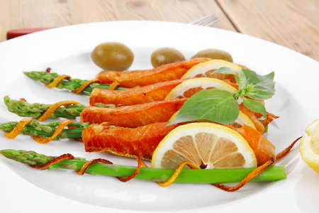 roasted salmon slices with asparagus lemon fried orange peel green olives and cutlery on white plate...