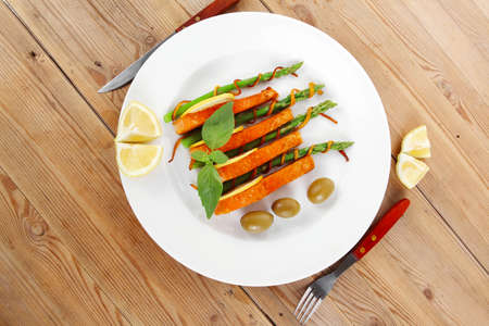 roasted salmon slices with asparagus lemon fried orange peel green olives and cutlery on white plate over wooden tableの写真素材