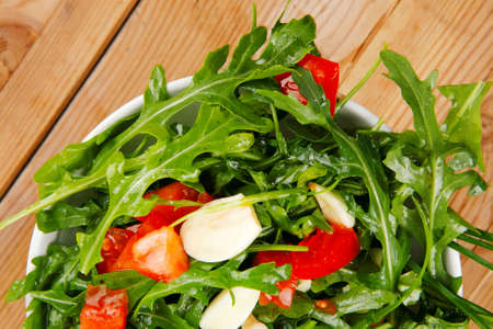 vegetable salad : green salad with raw tomato and garlic in white bowl over wood served with cutleryの写真素材