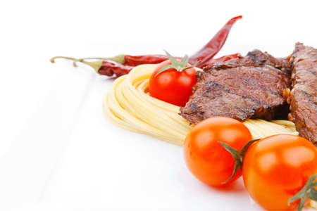 grilled beef fillet with pasta and tomatoes on white plate isolated over white backgroundの写真素材