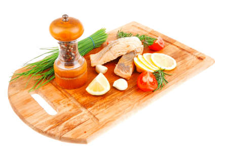 savory sea fish entree : roasted salmon fillet with green onion, red cherry tomatoes pieces, glass pepper grinder, rosemary twigs and lemon on wooden board isolated on white backgroundの写真素材
