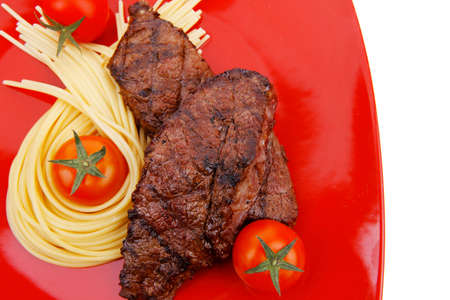 meat grilled beef steak with pasta and tomatoes on red plate isolated over white backgroundの写真素材