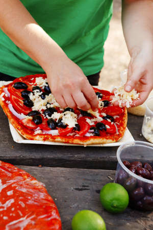 making hand made pizza with olives and tomatoes on wooden table on picnicの写真素材