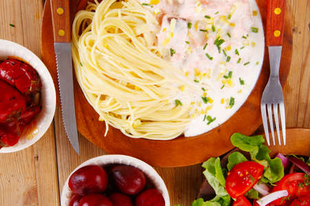 mediterranean cuisine: fresh rose wild salmon baked in cream cheese sauce with italian pasta and red hot pepper on wooden dish over table with vegetable saladの写真素材