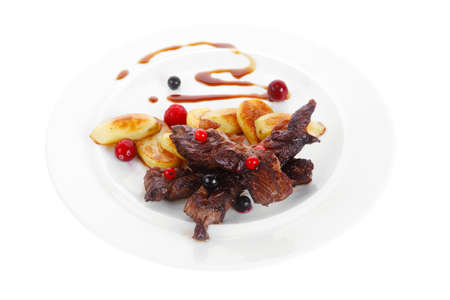 grilled beef meat with berries fried potatoes and cherry under sweet honey sauce on white plate isolated over white backgroundの写真素材