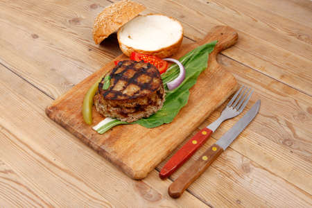 extra thick hot beef meat hamburger lunch on wooden plate with tomatoes and salad over wooden  table with cutlery and fresh sweet bunの写真素材