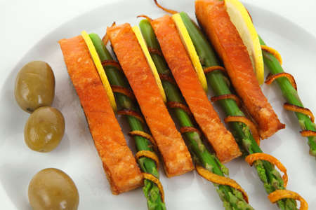 grilled salmon slices with asparagus lemon green olives and fried orange peel on big plate isolated over white backgroundの写真素材